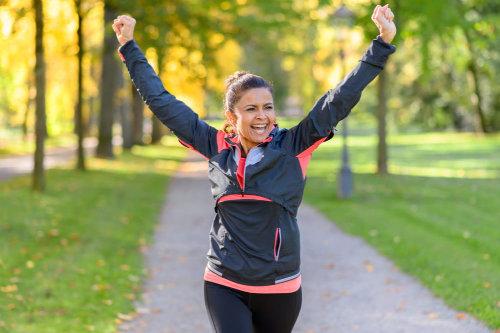 Woman jogging through the park with her hands triumphantly held high